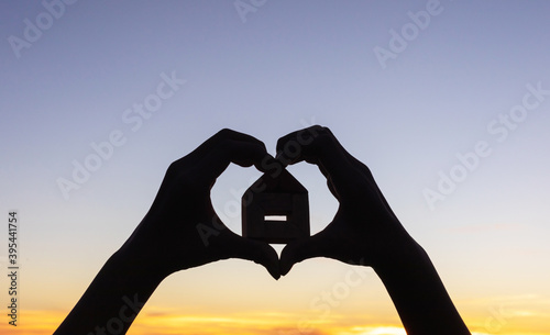 Silhouette hands making a heart shape with wooden house on sunset sky