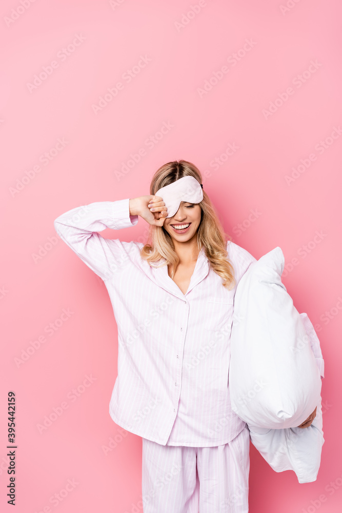 woman in blindfold and pajamas holding pillow on pink background woman in blindfold and pajamas holding pillow on pink background