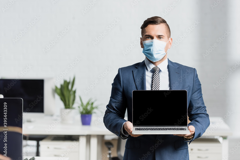 Front of businessman holding laptop with blank screen with blurred office on background Front of businessman holding laptop with blank screen with blurred office on background