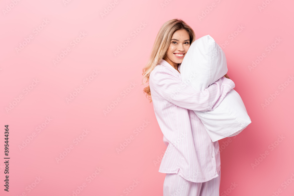woman in pajamas smiling at camera while holding pillow on pink background woman in pajamas smiling at camera while holding pillow on pink background