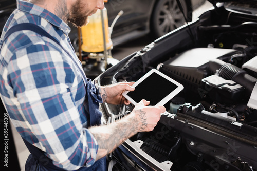 cropped of technician holding digital tablet near car engine compartment