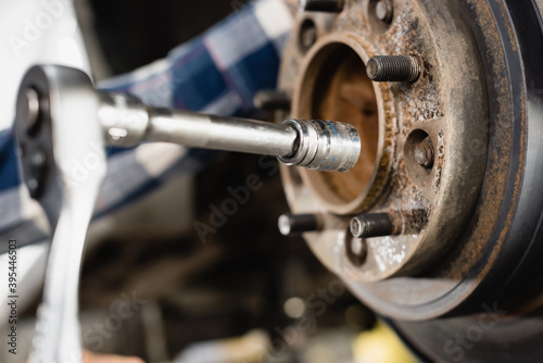 close up view of wheel hub and wrench in hands of mechanic on blurred 