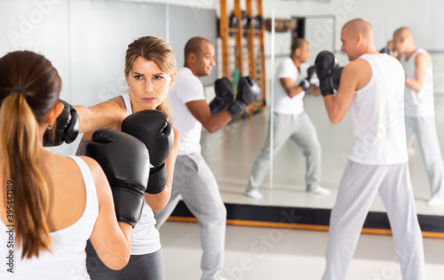 Determined young woman mastering self defense techniques, practicing punches at boxing gym