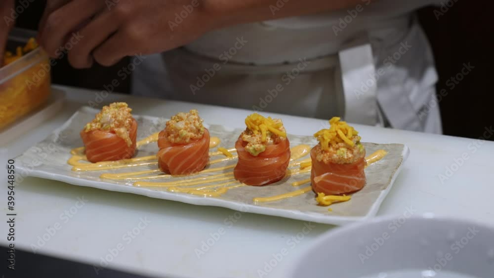 Close up of Professional male chef hand decorate salmon sushi roll on serving plate to customer. Chef preparing delicious sushi menu fish with rice on open kitchen counter bar in japanese restaurant Close up of Professional male chef hand decorate salmon sushi roll on serving plate to customer. Chef preparing delicious sushi menu fish with rice on open kitchen counter bar in japanese restaurant