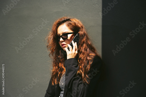 Fashion portrait of asian woman wearing sunglasses and black jacket using smartphone.