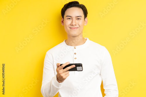 Asian businessman is holding his phone to watch a movie on a yellow background