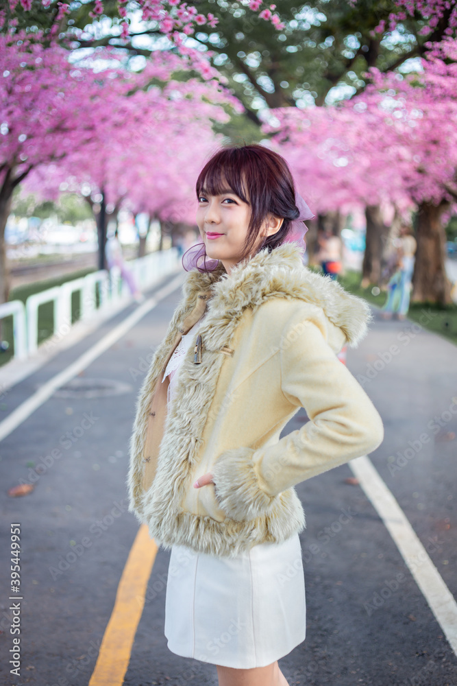 Happy young girl in a wool sweateron is enjoy and relax on a background with sakura cherry blossoms tree on vacation while spring in asian. Travel concept