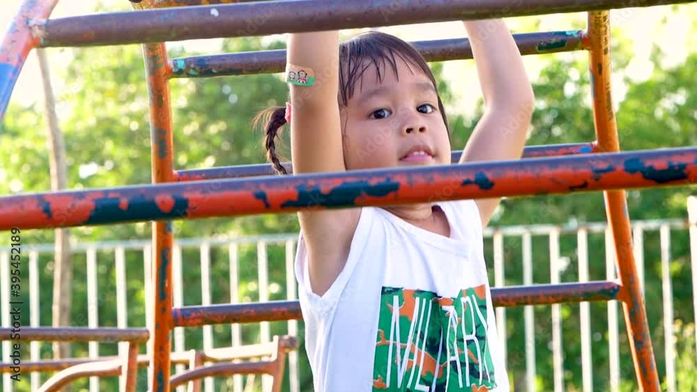 Happy little girl having fun playing on monkey bars at a playground. Outdoor activities on the children's summer vacation. Happy little girl having fun playing on monkey bars at a playground. Outdoor activities on the children's summer vacation.