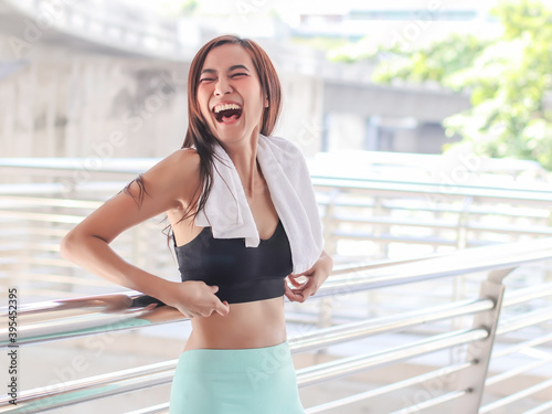 attractive Asian sportswoman in sportswear standing against bridge fence and laughing.