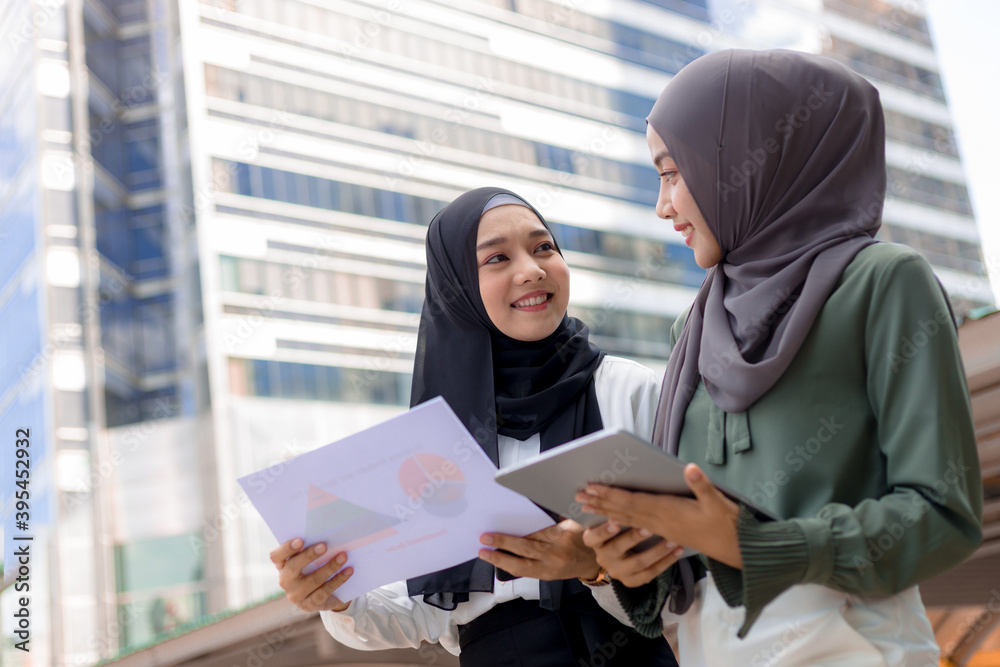 Two young Asian Muslim businesswomen stand together in a central business district. Two young Asian Muslim businesswomen stand together in a central business district.
