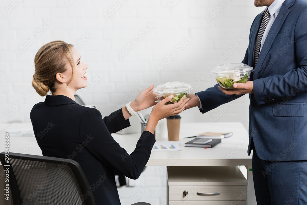 businesswoman taking plastic bowl with meal from colleague, sitting at workplace businesswoman taking plastic bowl with meal from colleague, sitting at workplace