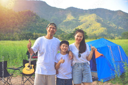 Young Asian family showing thumb up at camping site, father and mother with a son camping in a tent outdoors. © gamelover