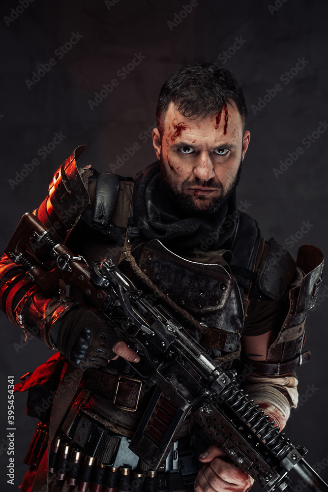 Dressed in dirty clothing with dark armour bearded survivor holding shotgun poses in dark background with serious face. Dressed in dirty clothing with dark armour bearded survivor holding shotgun poses in dark background with serious face.