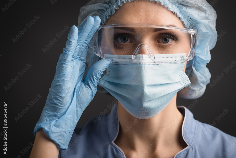 nurse in blue medical cap and mask adjusting goggles while looking at camera isolated on dark grey, stock image nurse in blue medical cap and mask adjusting goggles while looking at camera isolated on dark grey, stock image