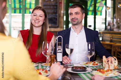 Smiling friends are drinking wine and eating in restaurant.