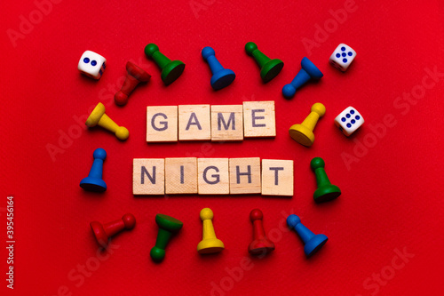 Wooden block lettering "Game night" on a red texture background surrounded by yellow, blue, green and red game chips and game cubes: Board game background