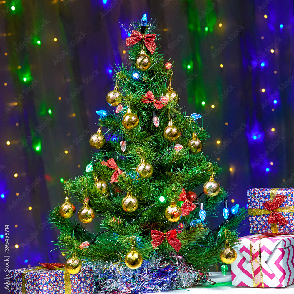 Gifts near a beautifully decorated Christmas tree against a background of bright lights