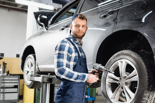  technician looking away while holding pneumatic wrench near wheel of lifted car