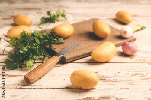 Raw potatoes with knife and cutting board on wooden table