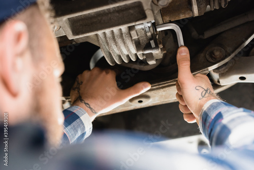 mechanic repairing bottom of lifted car with wrench on blurred 