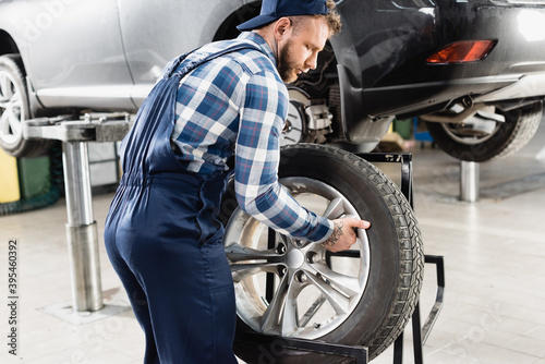 repairman in overalls taking wheel near auto raised on car lift, stock image