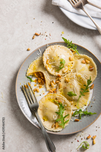 Fresh homemade pumpkin ravioli tortelloni parcels on a plate topped with pine nuts, parmesan and rocket