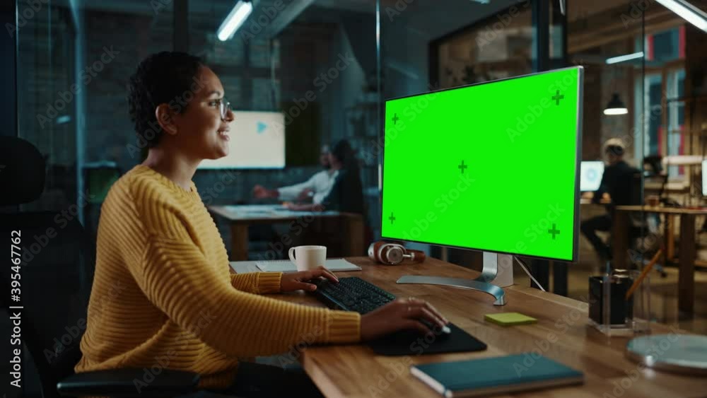 Young Multiethnic Specialist Working on Desktop Computer with Green Screen Mock Up Display in Creative Office. Beautiful Diverse Female Manager with Short Hair and Glasses is Wearing a Yellow Jumper. Young Multiethnic Specialist Working on Desktop Computer with Green Screen Mock Up Display in Creative Office. Beautiful Diverse Female Manager with Short Hair and Glasses is Wearing a Yellow Jumper.