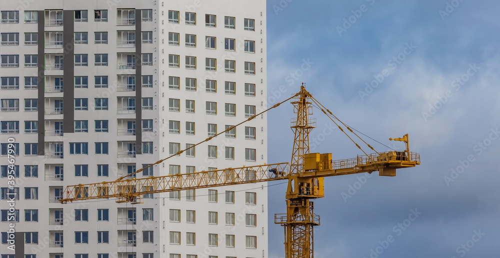 The top of the tower crane on the background of the building and the sky with clouds