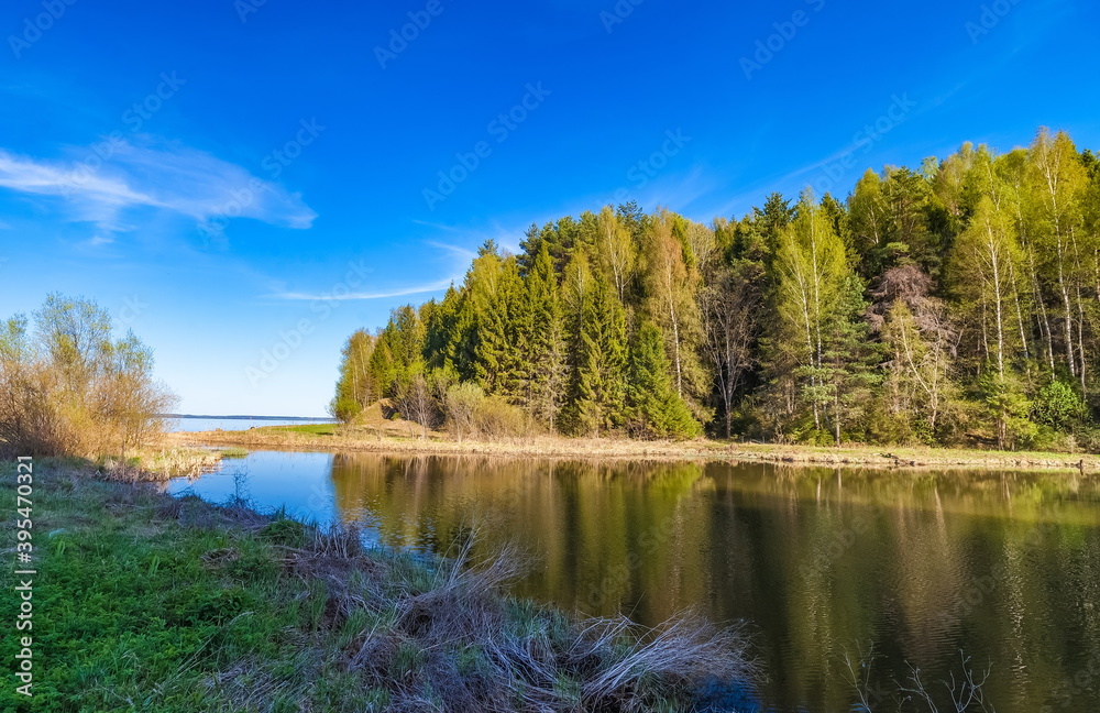 River flowing into a large river and trees against the blue sky in summer