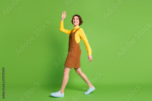 Full length profile photo of stepping girl waving palm wear yellow shirt overall sneakers isolated green color background