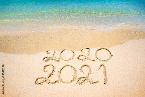 End of 2020 Happy New Year 2021, lettering on beach with wave and clear blue sea on sunny day. Handwritten inscription 2020 and 2021 on beautiful golden sand beach. New Years 2021 replace 2020 concept
