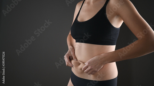 Cropped view of woman in black underwear massaging loose belly with her hands isolated on grey. Skin care and wight loss concept. © Tatsiana