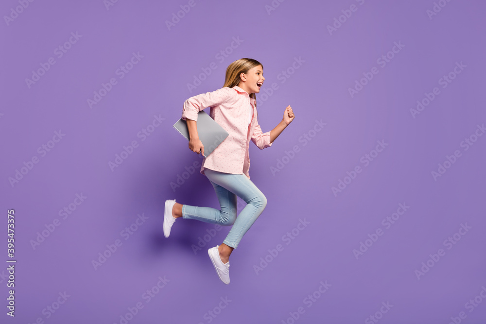 Full size profile photo of optimistic pretty girl jump run wear pink shirt jeans sneakers hold laptop isolated on violet background