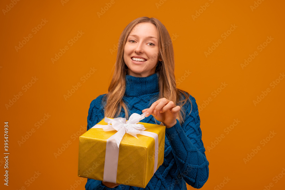 Portrait of a happy young woman holding gift decorated with ribbon. Studio shot, yellow background Portrait of a happy young woman holding gift decorated with ribbon. Studio shot, yellow background