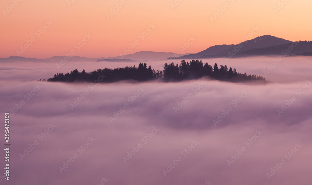 Sunset hidden behind clouds and fog over hills, bright yellow sun on colorful cloudscape, blue violet orange sky.