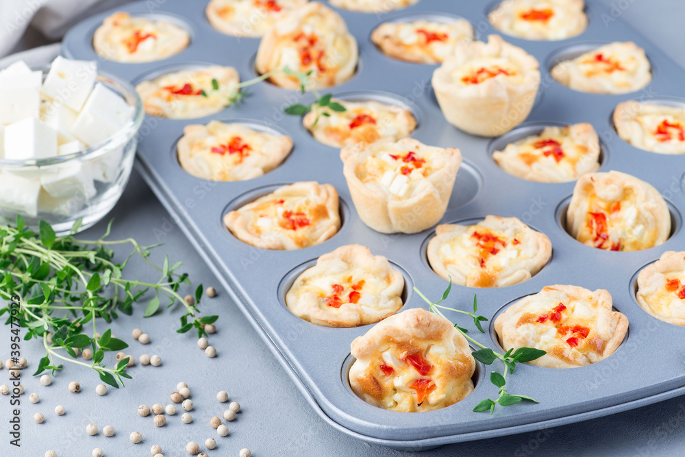 Mini quiche muffins with feta cheese, fried onion, thyme and red bell pepper, in a baking form, horizontal