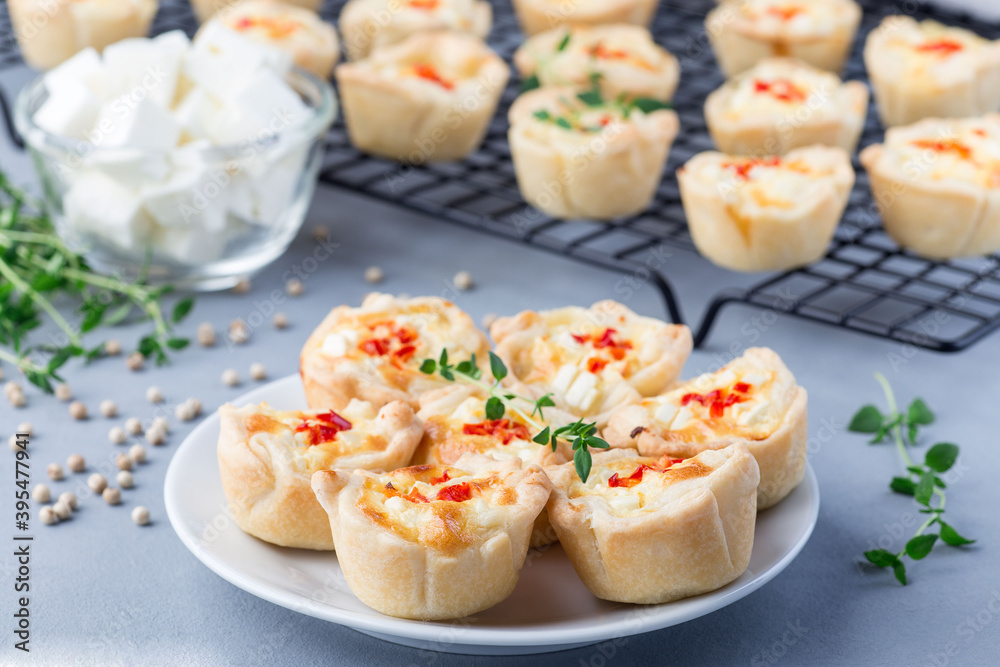 Mini quiche muffins with feta cheese, fried onion, thyme and red bell pepper, on a plate and cooling rack, horizontal