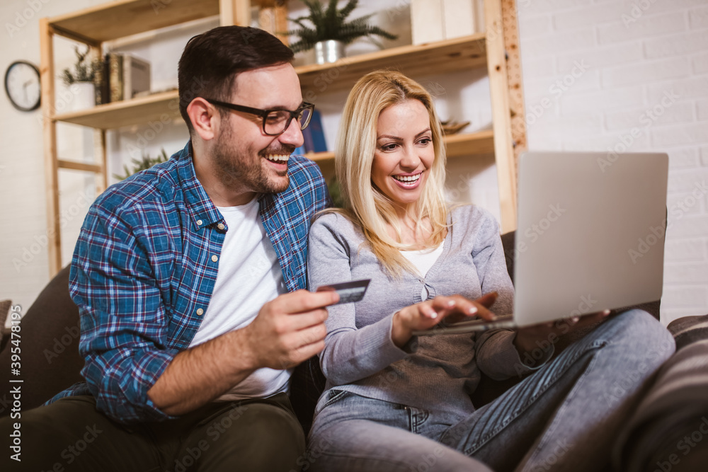 Happy couple communicating while using credit card and laptop for online shopping at home. Happy couple communicating while using credit card and laptop for online shopping at home.