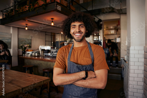Handsome young male waiter wearing apron standing with crossed arms in cafe looking at camera photo
