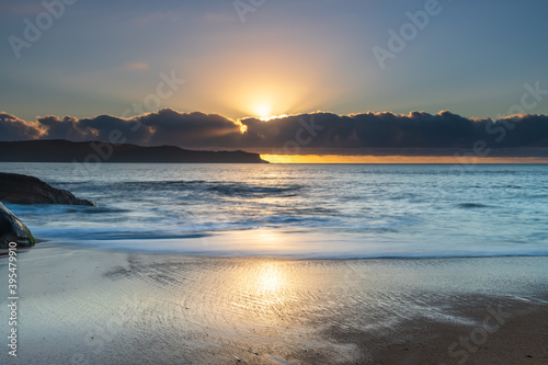 Sunrise by the sea with cloud bank and sun rays on the horizon