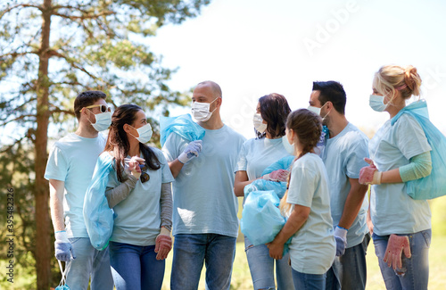 volunteering, health and ecology concept - young volunteers wearing face protective medical masks for protection from virus disease with garbage bags talking outdoors