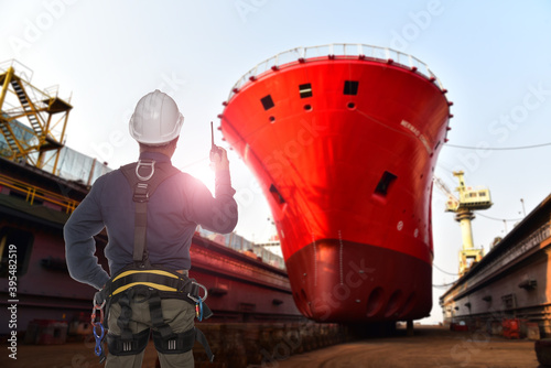 Safety workers standing in floating dry dock yard wearing equipment safety helmet and safety full harness during ship repairing and maintenance in shipyard.