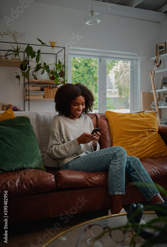 Obraz na plátně Happy african female relaxing at home browsing and typing on smartphone
