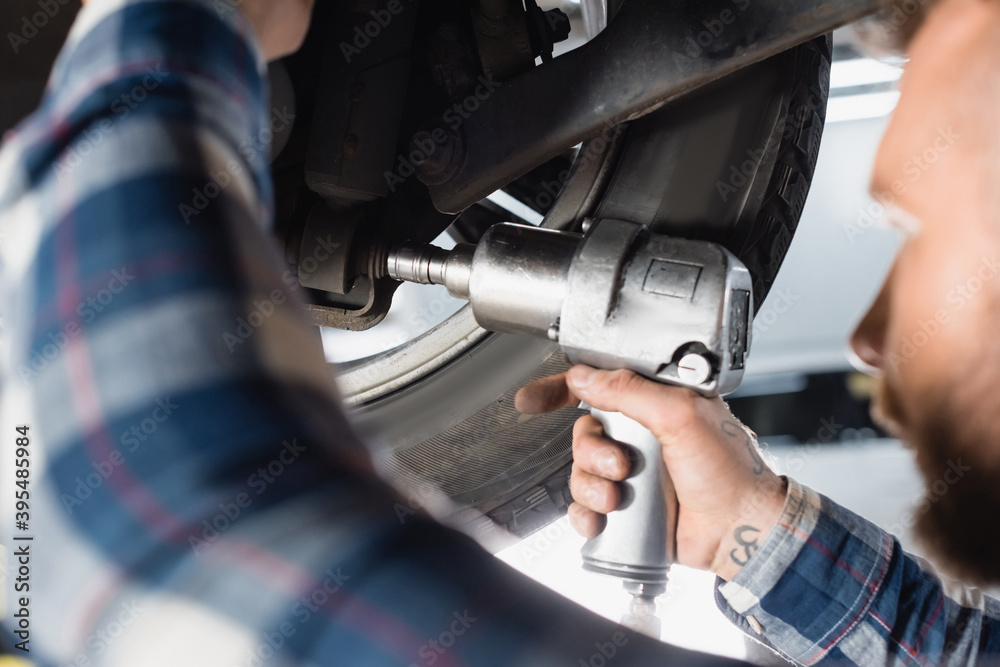 cropped of technician adjusting car wheel with pneumatic wrench on blurred foreground