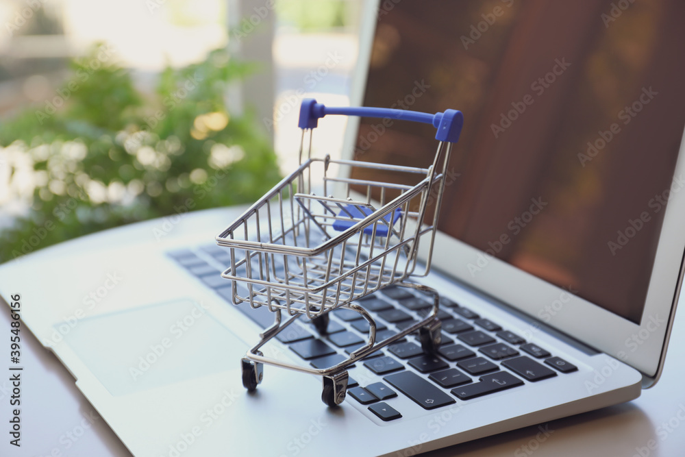 Internet shopping. Laptop with small cart on table indoors, closeup