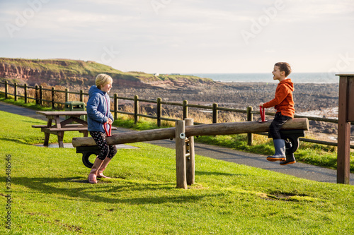 A young brother and sister playing on a seesaw in a park at Crail, Fife, Scotland. This park is on the coastal trail and is in a very beautiful location. photo