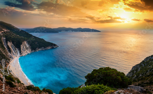 The famous Myrtos beach on the Greek island of Kefalonia, Ionian Sea, during a summer sunset with fluorescent, blue sea © moofushi