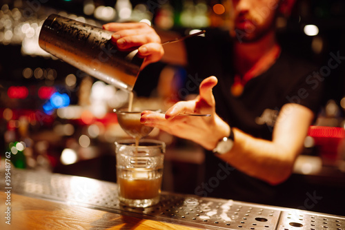 Close up detail of bartender makes a cocktail in a nightclub. Professional bartender pourring from a shaker through the sieve to a glass on the bar counter. Party  celebration  drink  holidays.