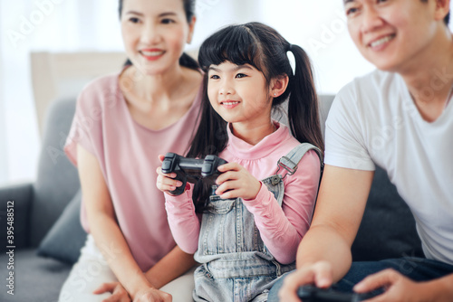 Playful asian family (mother, father, child daughter) playing video games together in a living room.