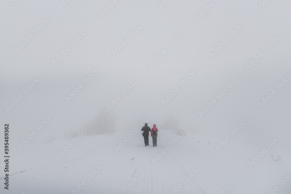 Two tourists walking in a snowstorm among snow and fog. Very soft selective focus.